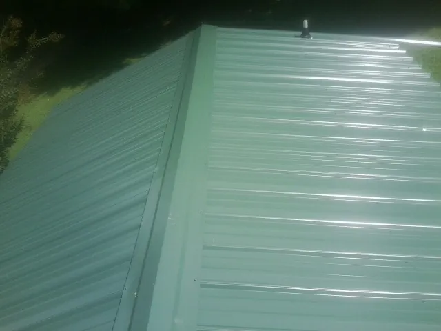 New green metal panels meeting at the ridge of a roof — Flat Roof Repair work by our crew in Maysville