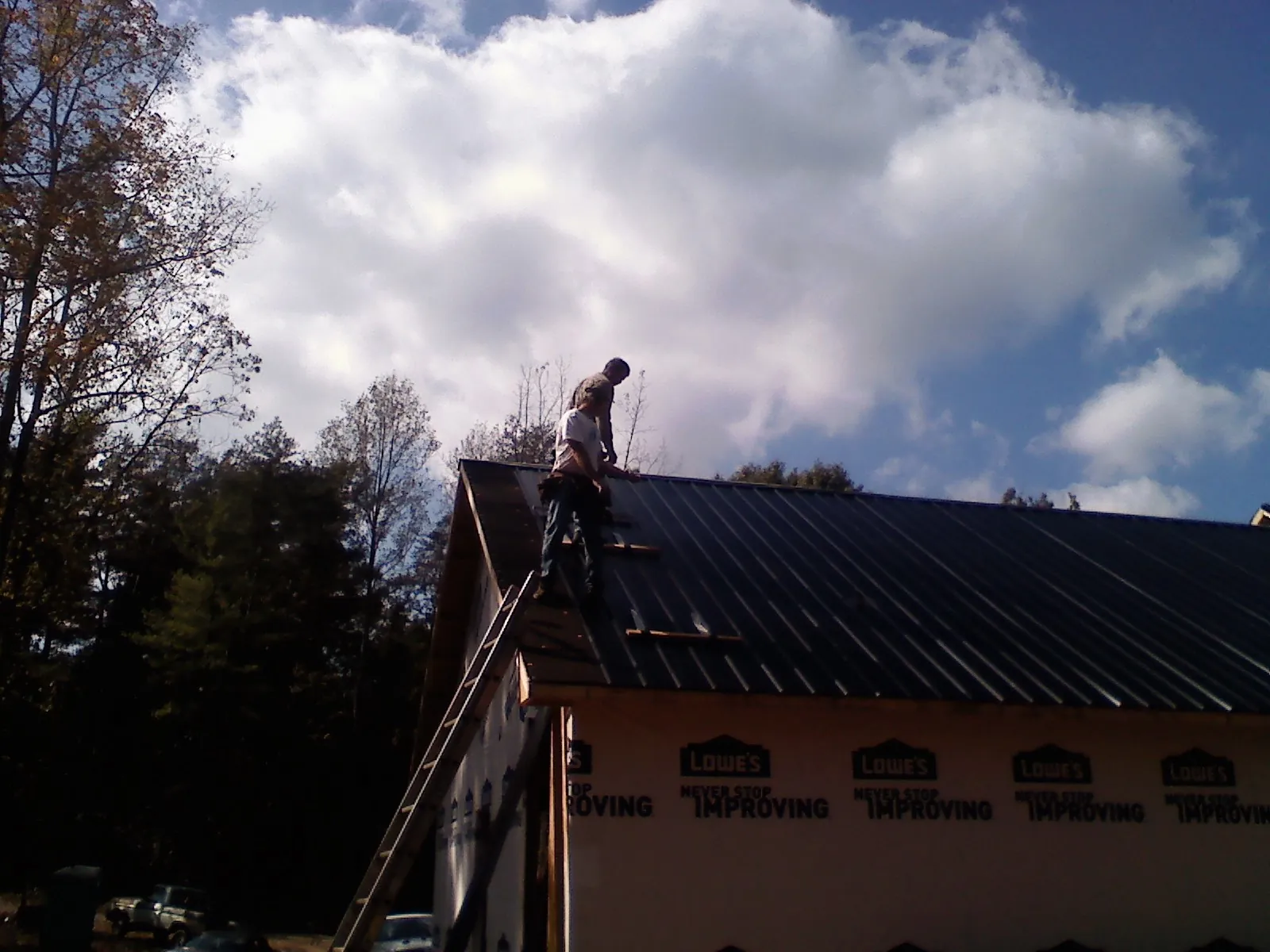Roofer fastening dark metal panels high against a cloudy sky, from a Roof Inspection job in Maysville
